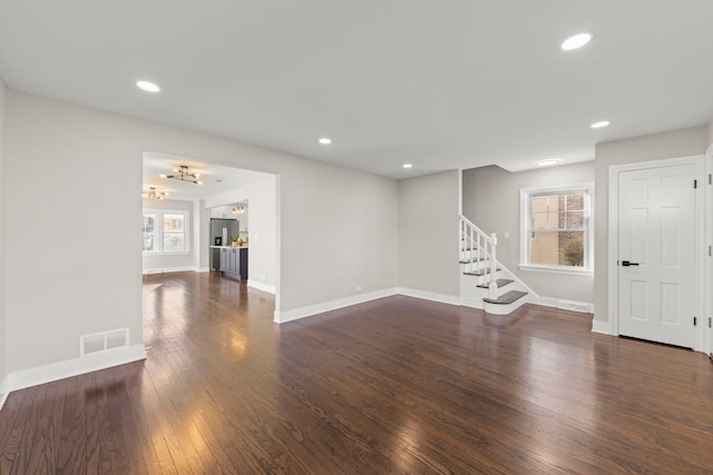 unfurnished living room featuring a wealth of natural light, visible vents, wood finished floors, and stairs