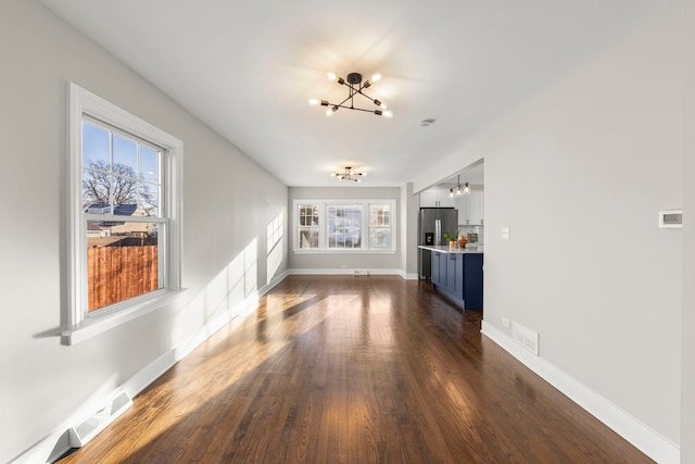 unfurnished living room featuring dark wood-style floors, plenty of natural light, visible vents, and an inviting chandelier