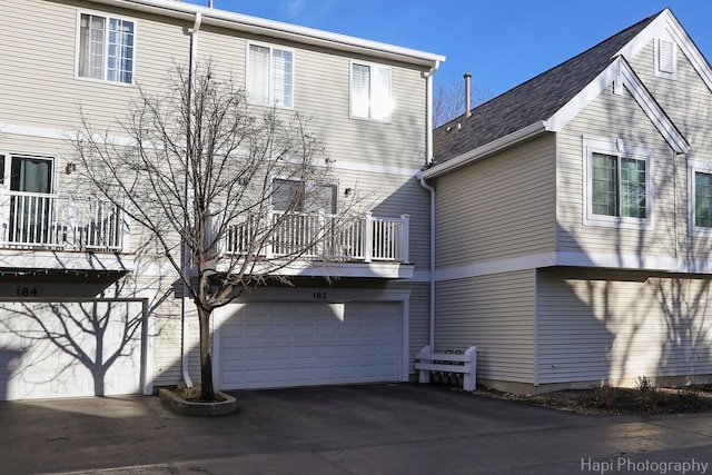 back of house featuring a garage, a balcony, and aphalt driveway