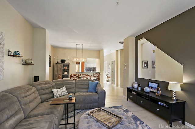 living room featuring visible vents, light wood-style flooring, and an inviting chandelier