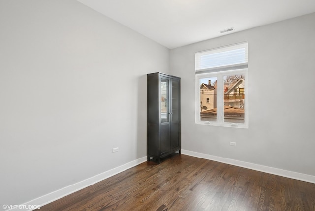 unfurnished room with dark wood finished floors, visible vents, and baseboards