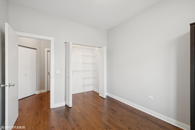 unfurnished bedroom with a closet, baseboards, and dark wood-style flooring