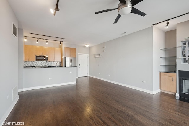 unfurnished living room with rail lighting, dark wood-type flooring, and a ceiling fan