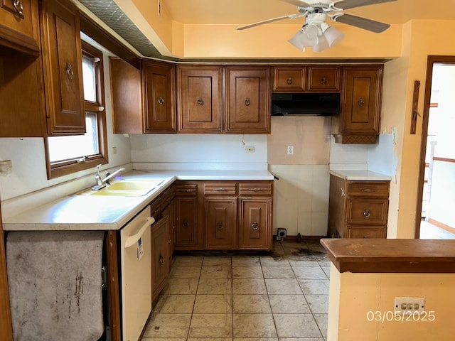 kitchen with under cabinet range hood, dishwasher, brown cabinetry, a ceiling fan, and a sink