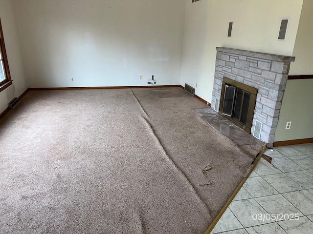 unfurnished living room with a stone fireplace, baseboards, and visible vents