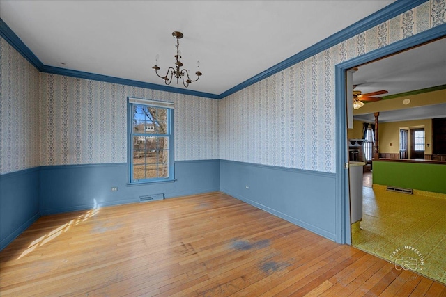 spare room with hardwood / wood-style floors, visible vents, a wainscoted wall, wallpapered walls, and crown molding