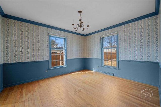 unfurnished room with visible vents, wallpapered walls, crown molding, wainscoting, and hardwood / wood-style flooring