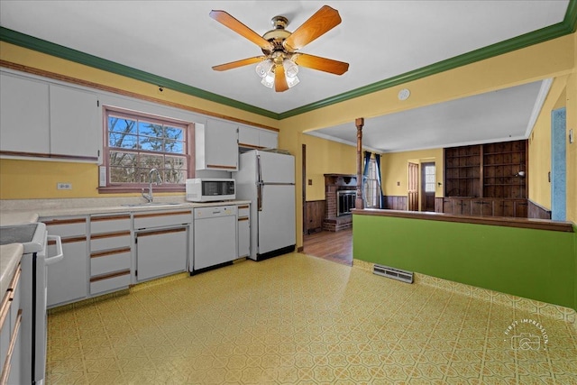 kitchen with white appliances, a wainscoted wall, visible vents, a sink, and crown molding