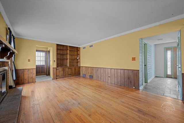 unfurnished living room with hardwood / wood-style floors, built in shelves, a wainscoted wall, crown molding, and a brick fireplace