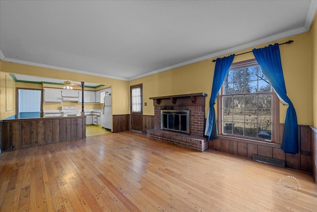 unfurnished living room featuring a wainscoted wall, visible vents, light wood-style flooring, ornamental molding, and a brick fireplace