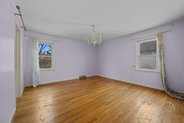 unfurnished room featuring a notable chandelier, baseboards, and light wood finished floors