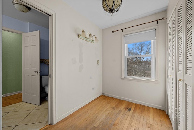 unfurnished bedroom with a closet, baseboards, and light wood-style flooring