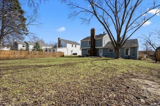 rear view of house featuring a lawn, a chimney, and fence