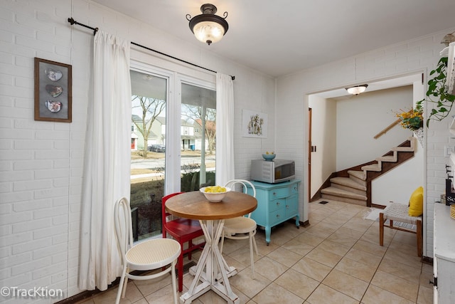 dining room with light tile patterned floors, brick wall, and stairs