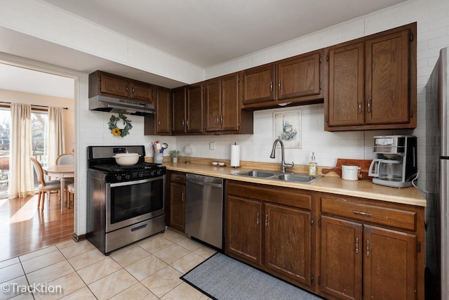 kitchen with under cabinet range hood, light countertops, appliances with stainless steel finishes, and a sink