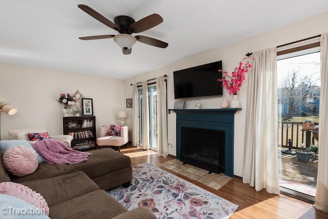 living area with ceiling fan, a fireplace with flush hearth, and wood finished floors