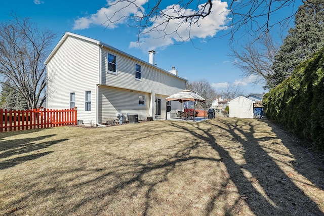 rear view of house featuring fence, a gazebo, a lawn, a chimney, and a patio area