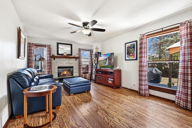 living area with a healthy amount of sunlight, a fireplace, ceiling fan, and wood finished floors