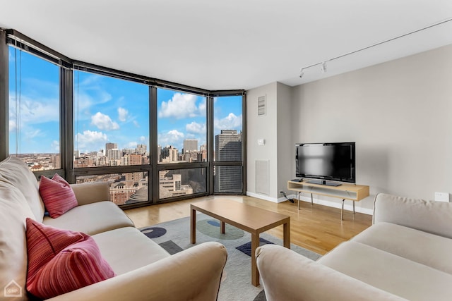 living area featuring wood finished floors, visible vents, baseboards, track lighting, and expansive windows