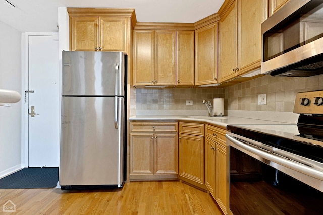 kitchen featuring light wood-type flooring, a sink, light countertops, appliances with stainless steel finishes, and tasteful backsplash