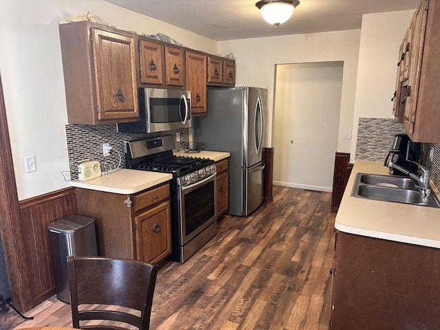 kitchen with dark wood-style floors, a sink, stainless steel appliances, light countertops, and wainscoting