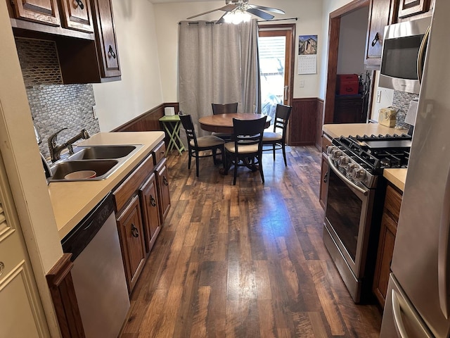 kitchen with dark wood-type flooring, light countertops, wainscoting, stainless steel appliances, and a sink