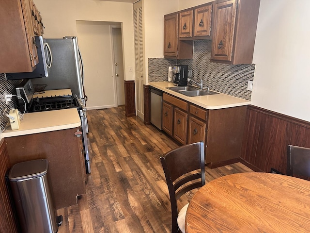 kitchen featuring a sink, appliances with stainless steel finishes, wainscoting, light countertops, and dark wood-style flooring