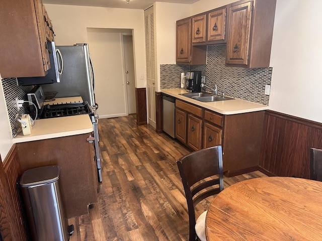 kitchen featuring light countertops, decorative backsplash, appliances with stainless steel finishes, dark wood-style floors, and a sink