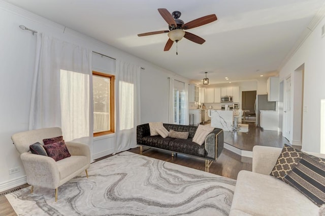 living area with ceiling fan, crown molding, baseboards, and wood finished floors