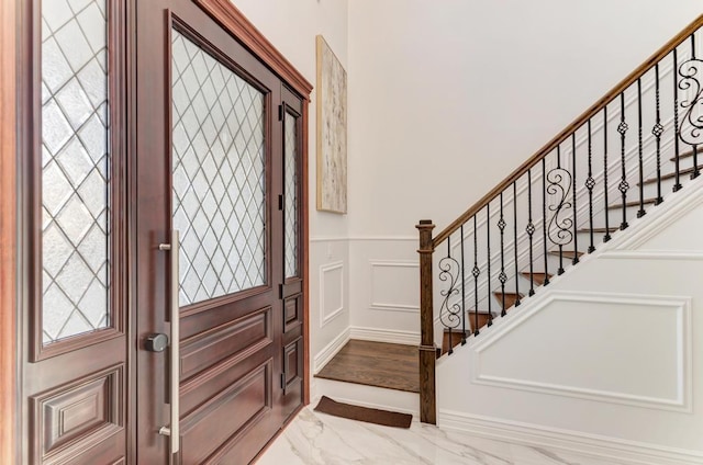 entrance foyer featuring a decorative wall, wainscoting, stairway, and marble finish floor