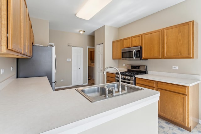 kitchen with a sink, appliances with stainless steel finishes, a peninsula, light countertops, and light floors