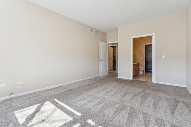 unfurnished bedroom with baseboards, visible vents, carpet floors, ensuite bath, and a walk in closet