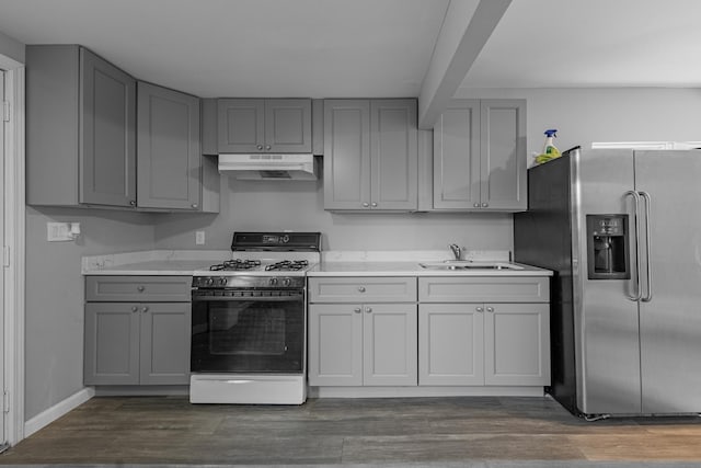 kitchen featuring gray cabinetry, under cabinet range hood, gas range oven, stainless steel fridge, and a sink