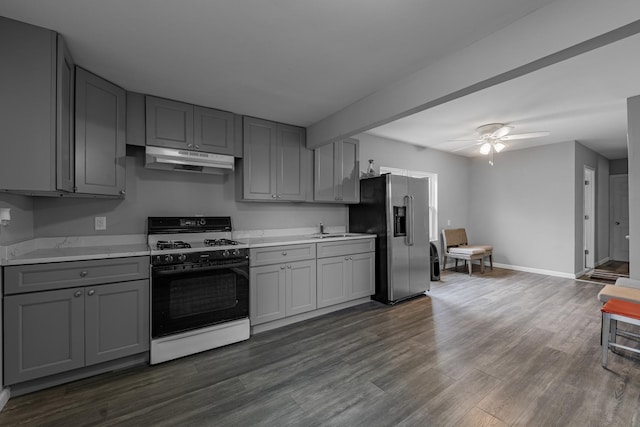 kitchen featuring gray cabinetry, under cabinet range hood, light countertops, range with gas stovetop, and stainless steel fridge