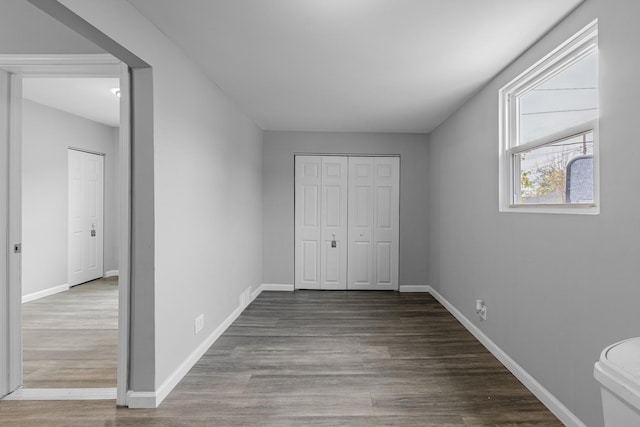 unfurnished bedroom featuring wood finished floors, baseboards, and a closet