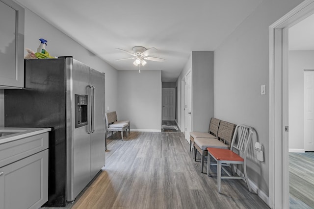 kitchen with a ceiling fan, wood finished floors, stainless steel fridge, and baseboards