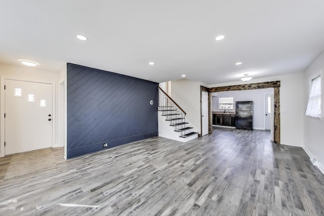 unfurnished living room featuring an accent wall, stairway, recessed lighting, and wood finished floors