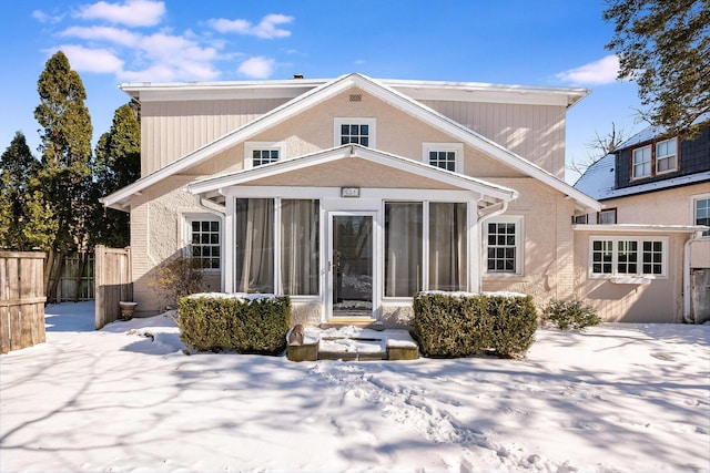 snow covered rear of property with a sunroom and fence