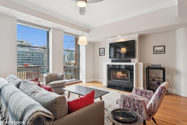 living room with wood finished floors, visible vents, baseboards, a fireplace with flush hearth, and ornamental molding