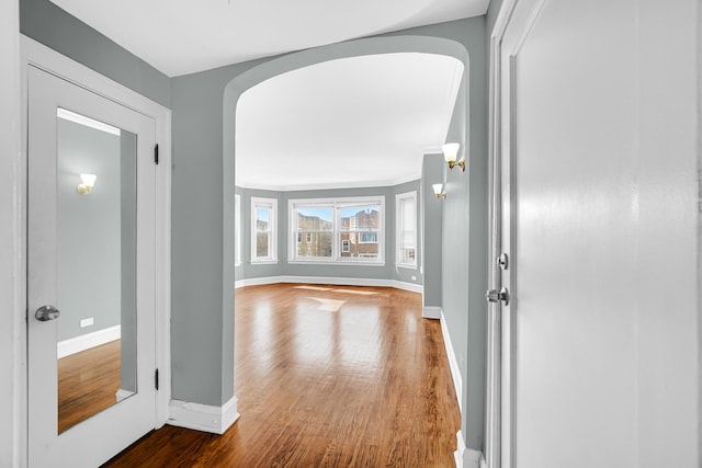 corridor with arched walkways, baseboards, and wood finished floors