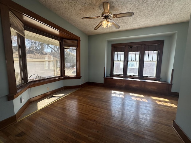 empty room featuring baseboards, dark wood-type flooring, a ceiling fan, and a textured ceiling