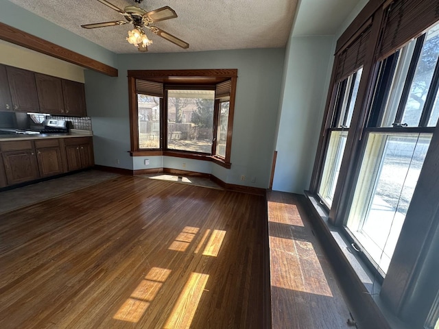 unfurnished dining area featuring a ceiling fan, baseboards, dark wood-style flooring, and a textured ceiling