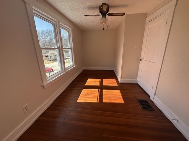 empty room with visible vents, a textured ceiling, baseboards, ceiling fan, and dark wood-style flooring