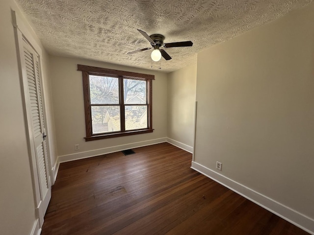 unfurnished bedroom with dark wood-style floors, visible vents, a textured ceiling, and baseboards