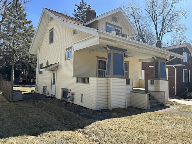 view of side of home with a balcony, a yard, a ceiling fan, and a chimney