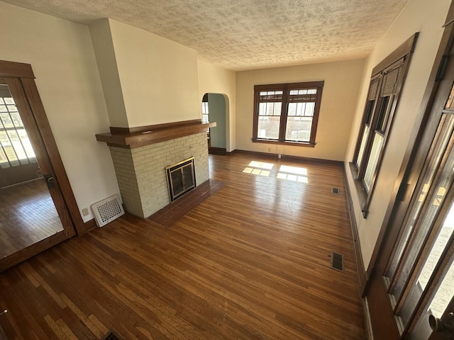 unfurnished living room featuring visible vents, dark wood-type flooring, baseboards, a fireplace, and a textured ceiling