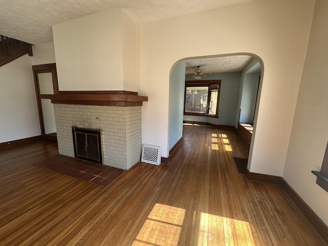 unfurnished living room with wood finished floors, visible vents, arched walkways, a textured ceiling, and a brick fireplace