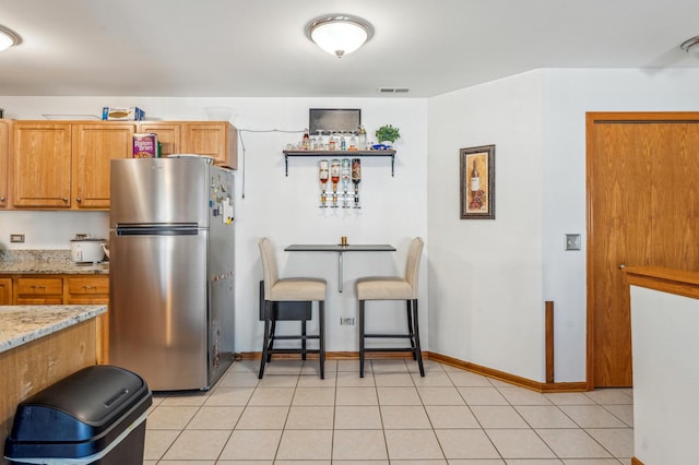 kitchen featuring light tile patterned floors, light stone countertops, visible vents, and freestanding refrigerator