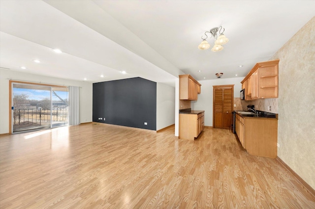 kitchen featuring light wood finished floors, open shelves, dark countertops, stainless steel microwave, and open floor plan