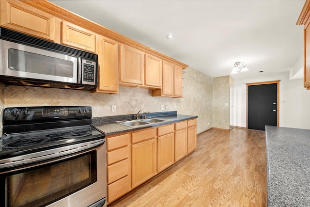 kitchen featuring dark countertops, light brown cabinets, appliances with stainless steel finishes, and a sink